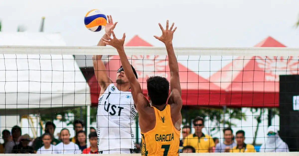 How to Play Beach Volleyball: Easy Beginner's Guide in 2024 1 How to Play Beach Volleyball: A male Beachvolleyball Player hitting a ball while another player wants to block