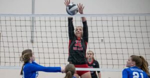 How to Play Volleyball for Beginners: A female volleyball player blocking a ball at the net