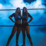These 30+ Partner Volleyball Poses Will Make You Go Viral! 4 Partner Volleyball Poses: two girls standing in front of a volleyball net with blue spotlight and smoke in the background